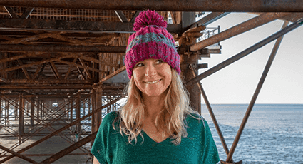 smiley blond long hair woman with purple striped bobble hat on under Brighton Palace pier